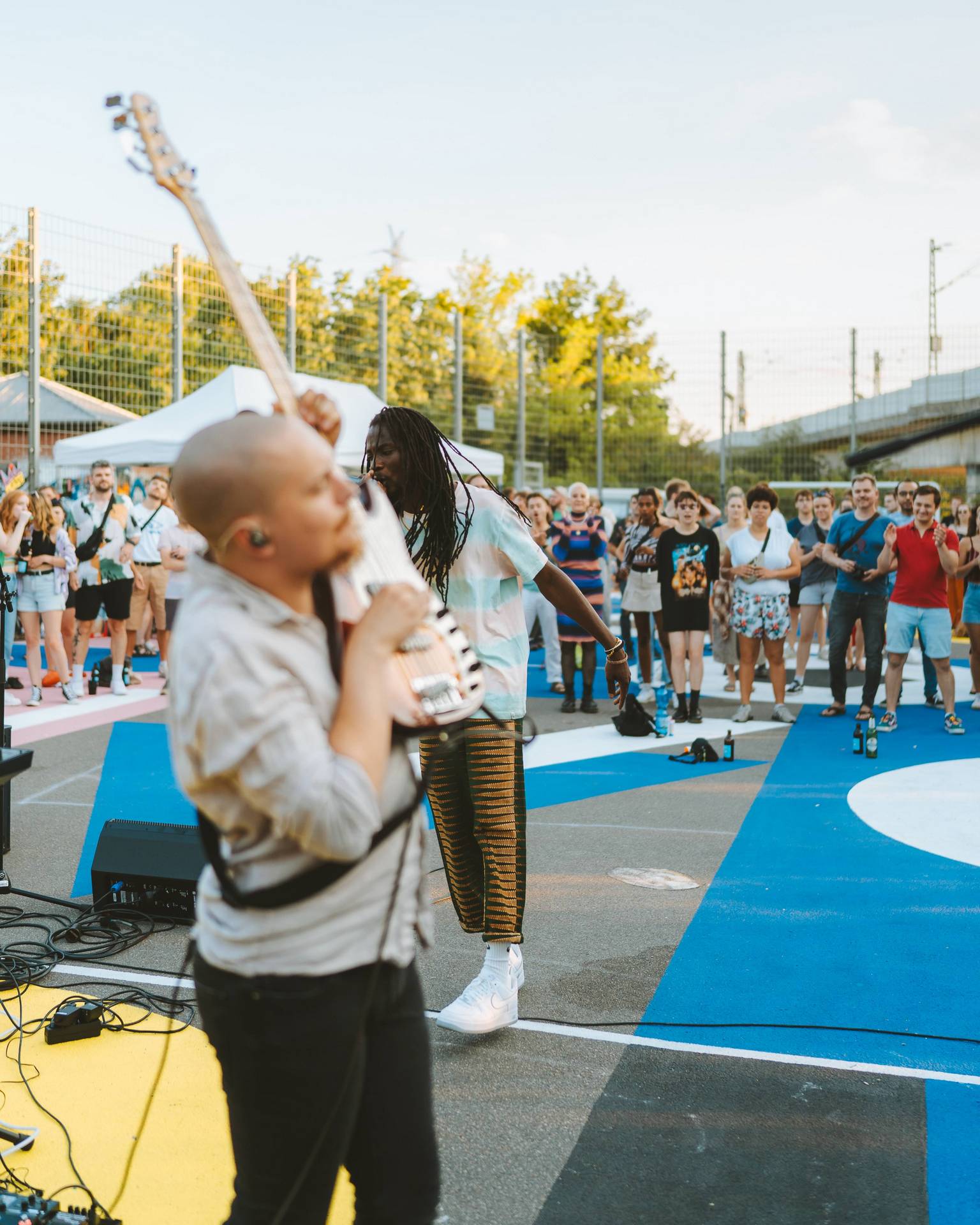 Fofana Jo perfoming in front of a crowd on a soccer field while his bass player Hannes Merten is holding his Bass really high for the end of the song